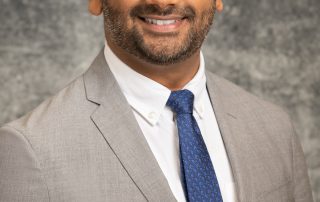 Male in gray suit, blue tie, and glasses