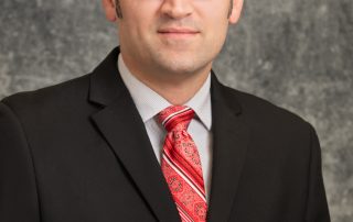 Male in a black suit, red tie, and glasses.