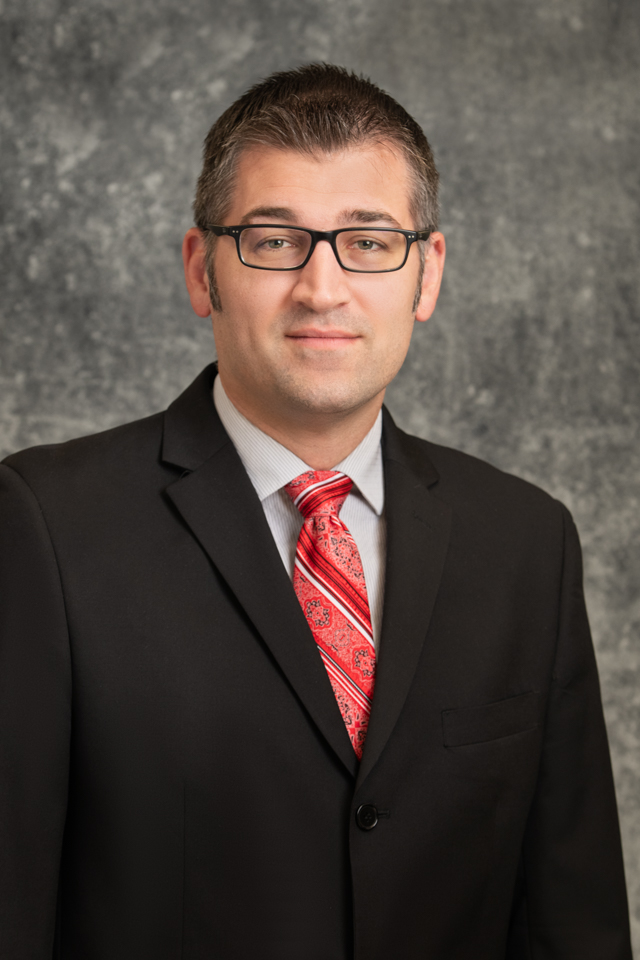 Randy Petersen Male in a black suit, red tie, and glasses.